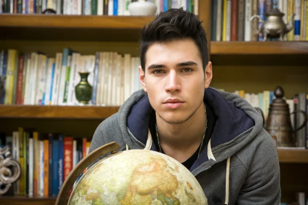 Handsome young man holding a globe indoors — Stock Photo, Image