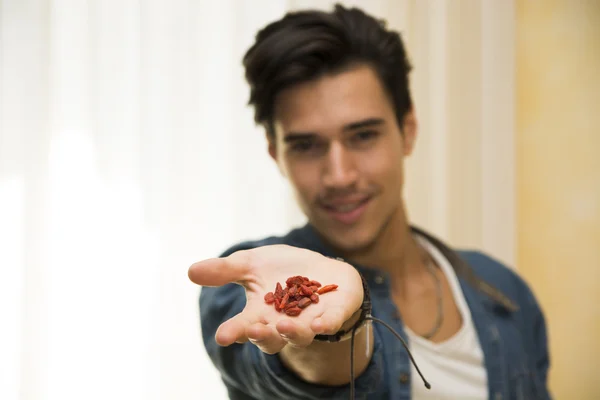 Smiling young man holding goji berries in his hand — Stock Photo, Image