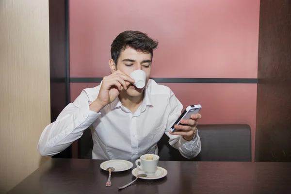 Člověk pije kávu při pohledu na telefon — Stock fotografie