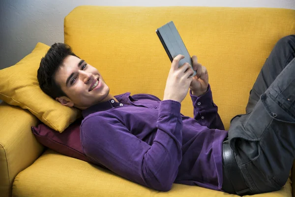 Man using tablet PC while laying on couch — Stock Photo, Image