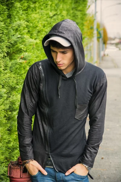 Atractivo joven en suéter negro con capucha permanente al aire libre —  Fotos de Stock