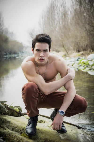 Handsome fit shirtless young man next to water pond or river — Stock Photo, Image