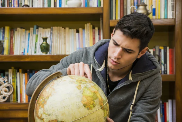 Handsome young man looking at a globe – stockfoto