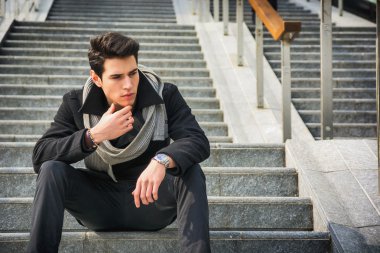 Uzun bir merdiven üzerinde oturan trendy yakışıklı adam