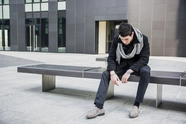 Moda hombre joven guapo sentado en el Banco de piedra —  Fotos de Stock