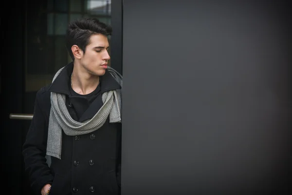 Trendy handsome young man standing against wall in urban environment — Stock Photo, Image