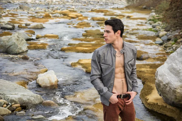 Young man next to river with open jacket — Stock Photo, Image