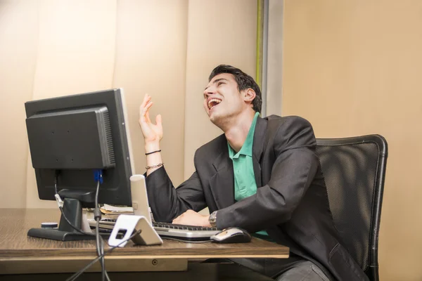Hombre de negocios joven sentado en su escritorio riendo — Foto de Stock