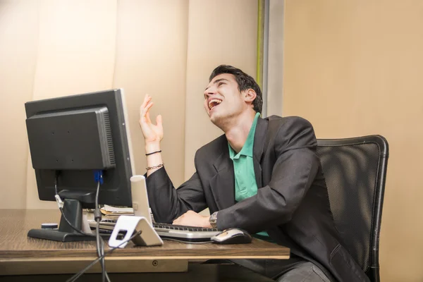 Jovem empresário sentado em sua mesa rindo — Fotografia de Stock