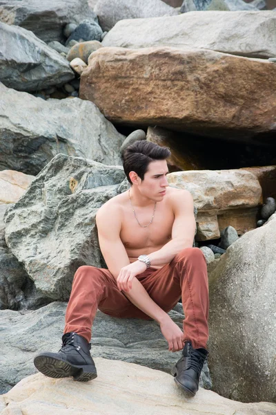 Bar överkropp ung man sitter utomhus på stenar, — Stockfoto