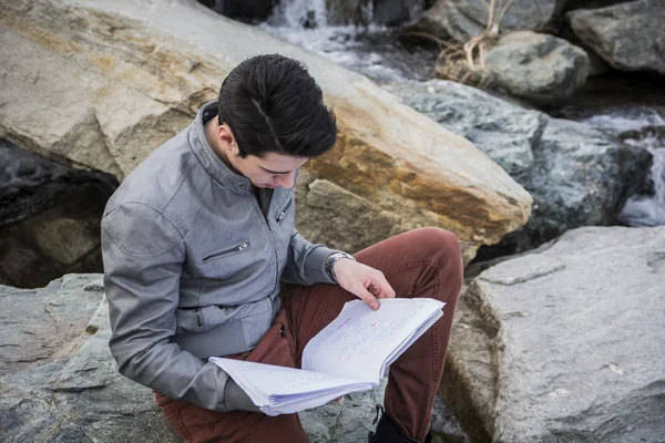 Estudante do sexo masculino a estudar ao ar livre, sentado sobre as rochas — Fotografia de Stock