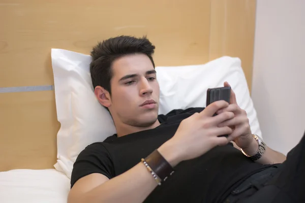 Knappe jongeman in bed typen op mobiele telefoon — Stockfoto