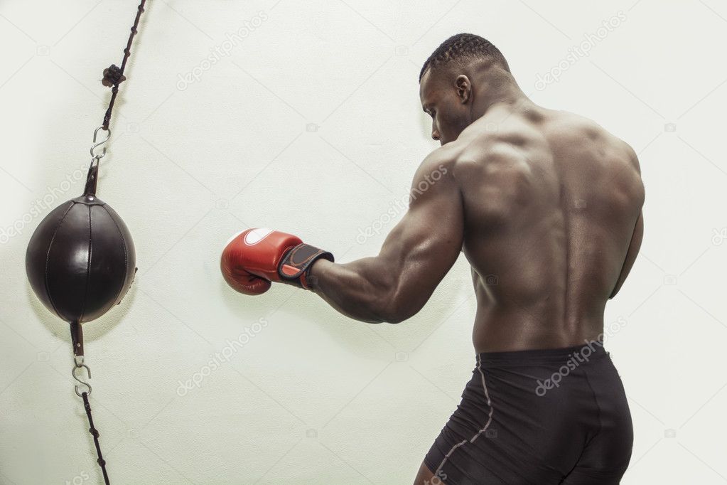 African male boxer punching ball wearing boxing gloves