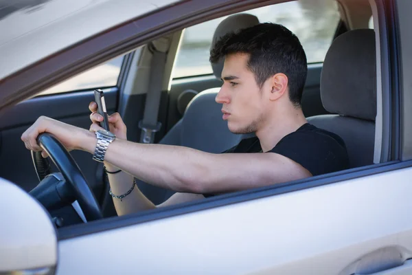 Молодой человек использует свой мобильный телефон за рулем автомобиля — стоковое фото