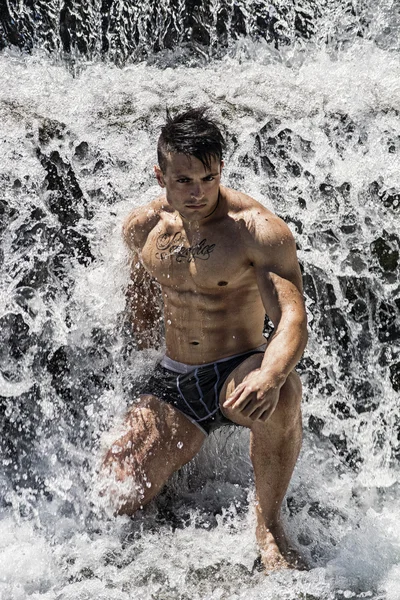 Attractive muscular shirtless young man under small waterfall — Stock Photo, Image