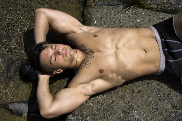 Handsome shirtless muscular young man sunbathing on rock — Stock Photo, Image