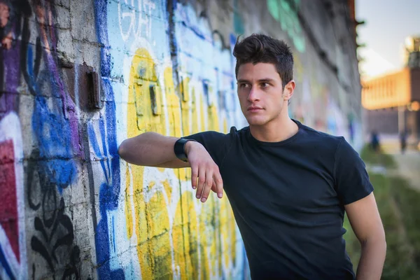 Привлекательный молодой человек, стоящий у красочной стены граффити — стоковое фото
