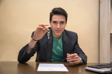 Young Male Agent Holding a Key at his Table clipart