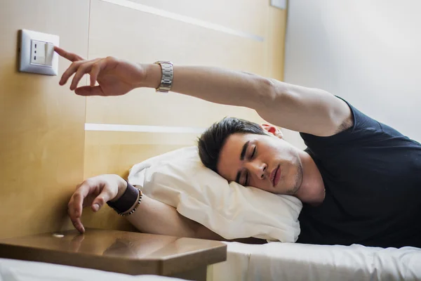 Fatigué Guy éteindre la lumière tout en étant allongé sur le lit — Photo