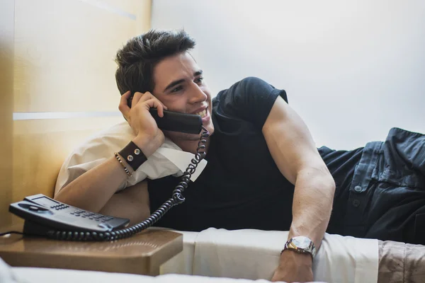 Sonriente joven tumbado en la cama y hablando por teléfono —  Fotos de Stock