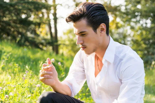 Attractive young man touching flowers in a forest — Stock Photo, Image