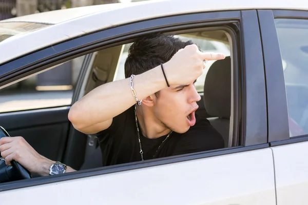 Hombre joven conduciendo un coche y mostrando el dedo medio — Foto de Stock