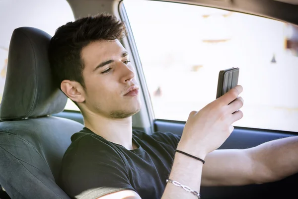 Hombre joven usando el teléfono móvil mientras conduce — Foto de Stock