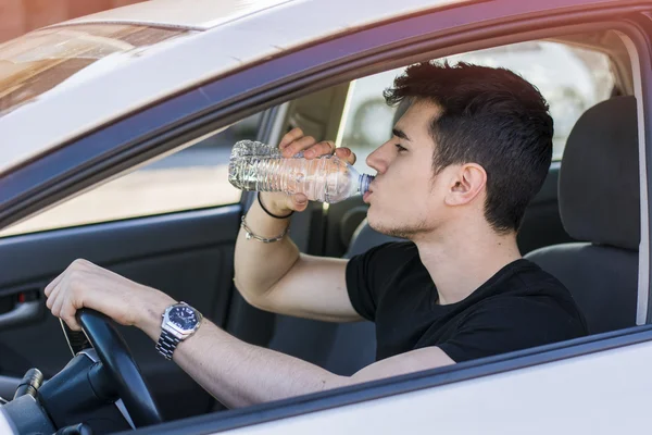 若い男運転の車、ボトルから水を飲む — ストック写真