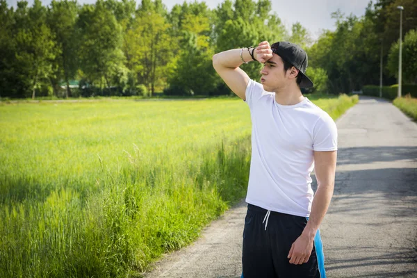Young man resting standing in middle of the road after running — Stock Photo, Image