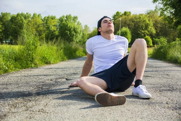 Knappe jonge man rust zittend op weg na het lopen — Stockfoto