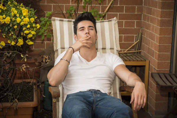 Pohledný tmavé vlasy mladý muž s cigaretou v balkon, v létě — Stock fotografie