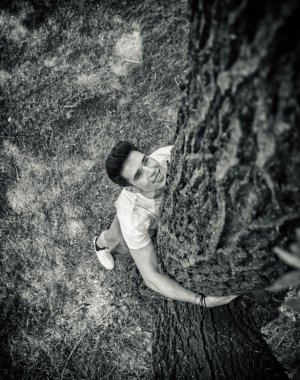 Genç adam bir ağaç sarılma ararken gülümseyen