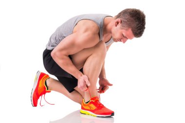 Yakışıklı genç bir adam diz çökmüş ve uygulamakla spor ayakkabı