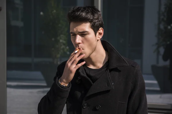 Young man smoking outside in urban setting — Stock Photo, Image