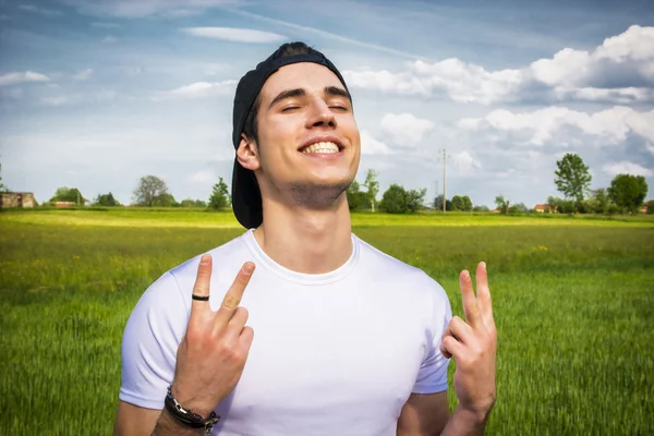 Young man at countryside, doing victory sign smiling — Stock Photo, Image