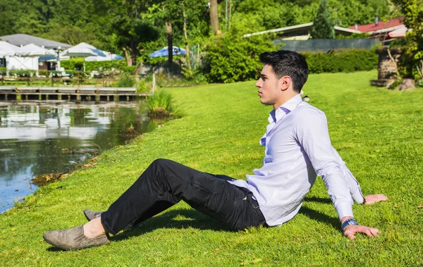 Hombre sentado en el césped junto a un lago — Foto de Stock