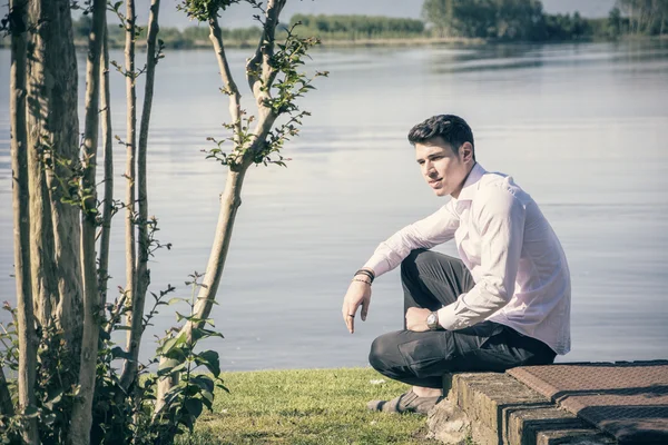 Hombre sentado en el césped junto al lago — Foto de Stock