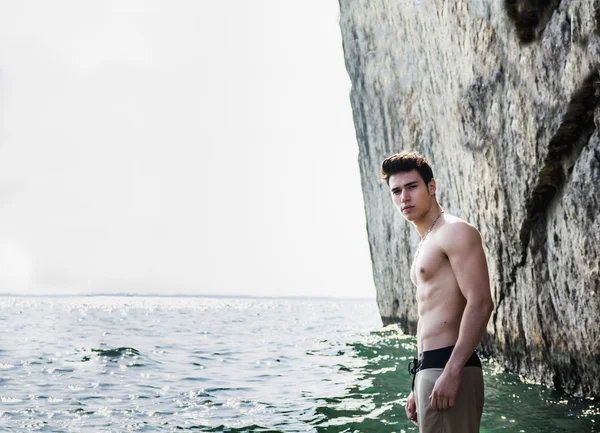 Young shirtless athletic man standing in water by ocean shore — Stock Photo, Image