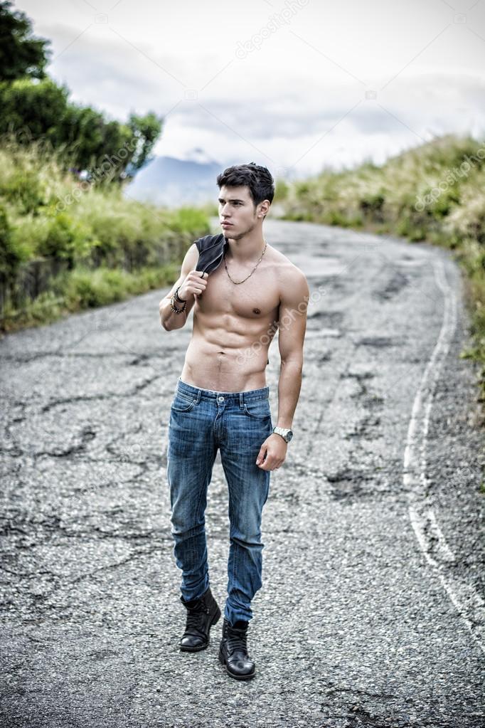 Shirtless muscular young man walking on rural road