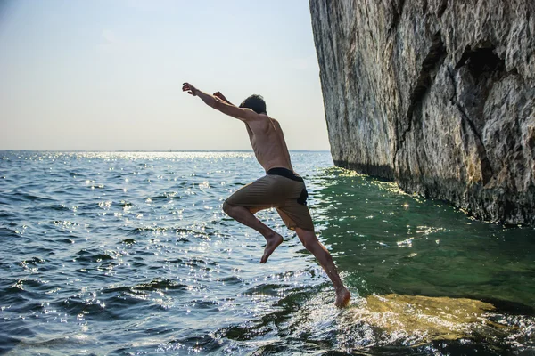 Košili sportovní mladík skákání ve vodě pobřeží oceánu — Stock fotografie