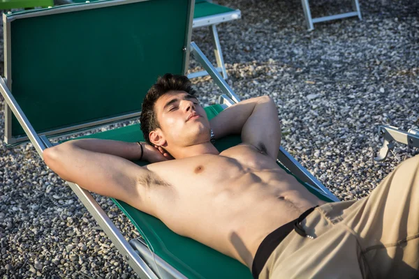 Jovem sem camisa tomando sol na espreguiçadeira na praia — Fotografia de Stock