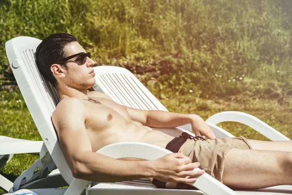 Jovem sem camisa tomando sol na espreguiçadeira na grama — Fotografia de Stock