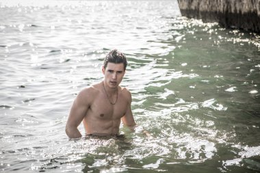 Okyanus kıyısında suda duran genç üstsüz atletik adam.