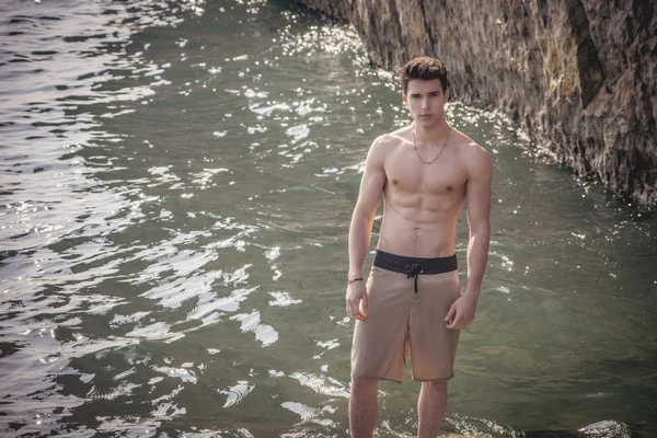 Young shirtless athletic man standing on rock by sea — Stock Photo, Image