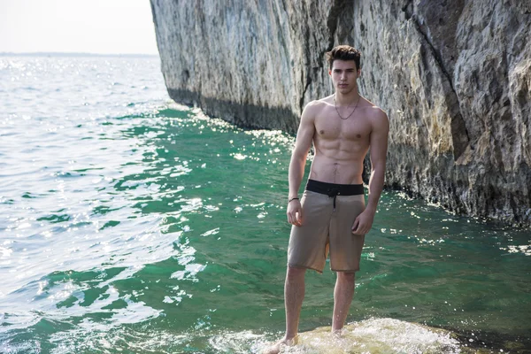 Young shirtless athletic man standing on rock by sea — Stok Foto