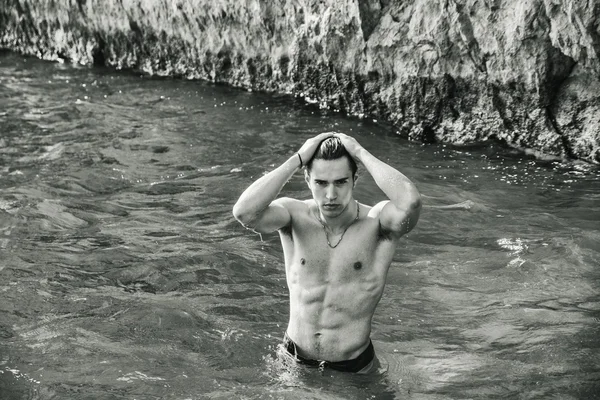 Young shirtless athletic man standing in water by ocean shore — Stock Photo, Image