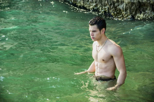 Mladý atletický muž bez košile stojící ve vodě u pobřeží oceánu — Stock fotografie