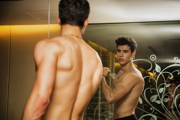 Hombre joven admirando los músculos bíceps en el espejo — Foto de Stock