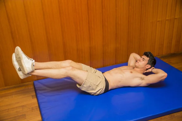 Bonito jovem fazendo exercícios abdominais no tapete — Fotografia de Stock