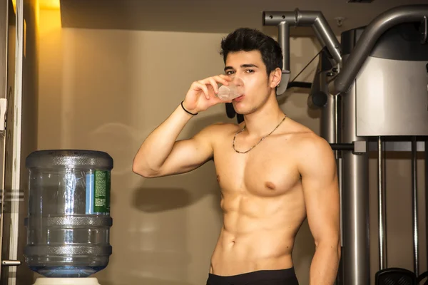 Attractive athletic young man drinking water in gym — Stock Photo, Image